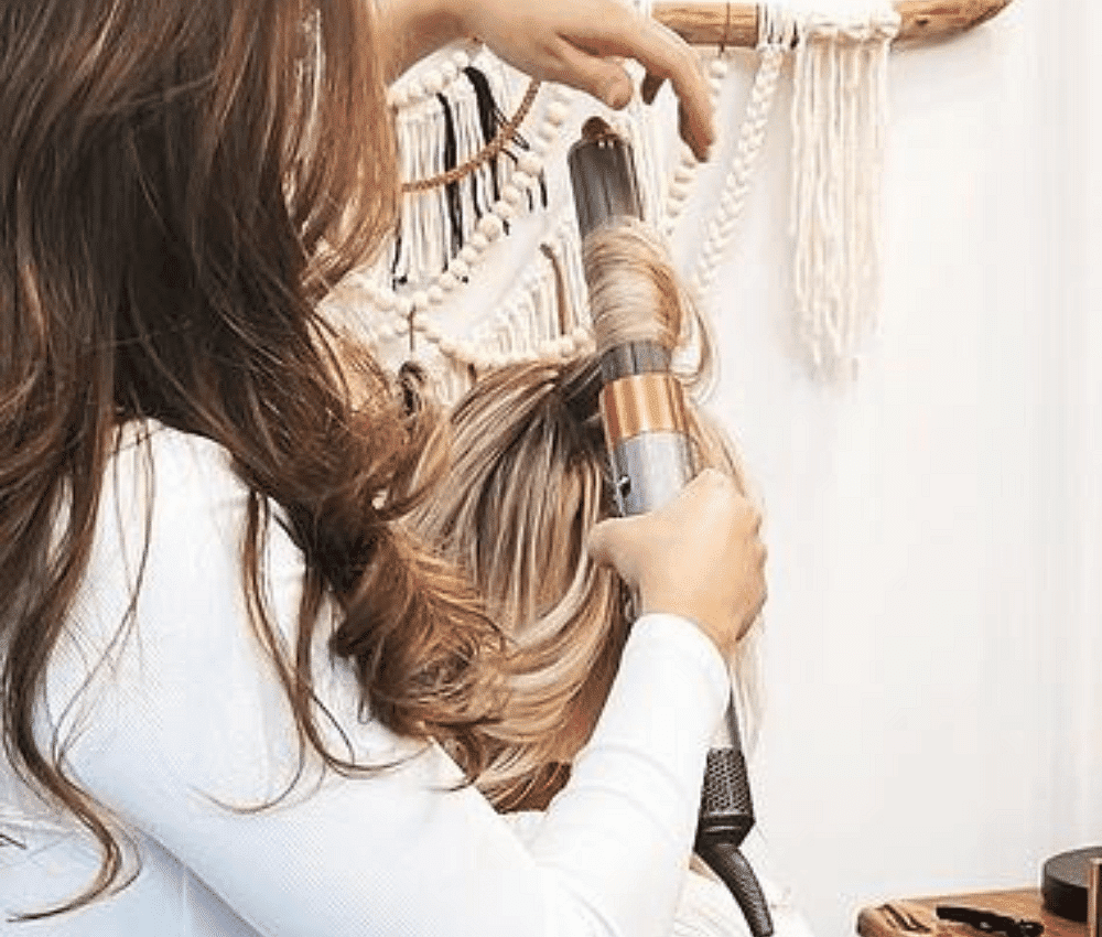 Stylist blow drying and curling wavy hair on blond seated model facing away